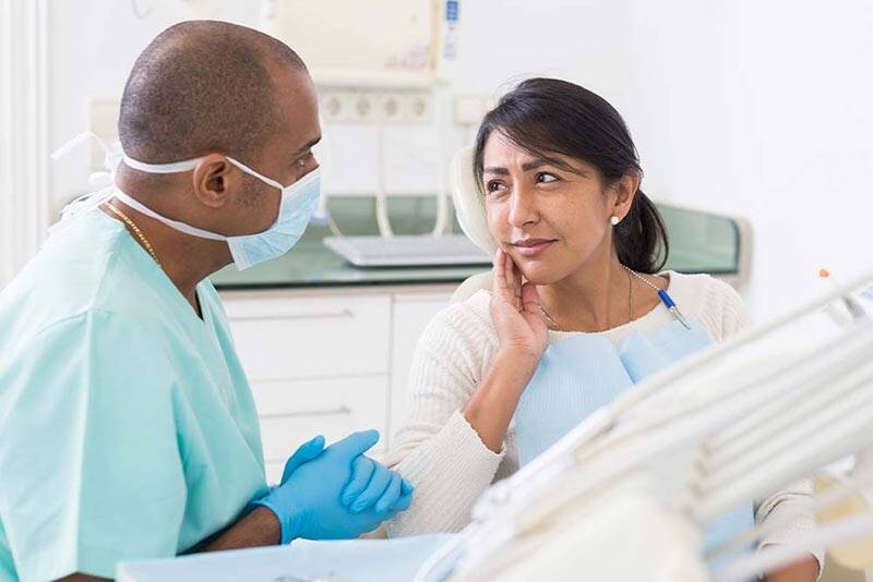 Female patient holding her gums while discussing dental concerns with the dentist